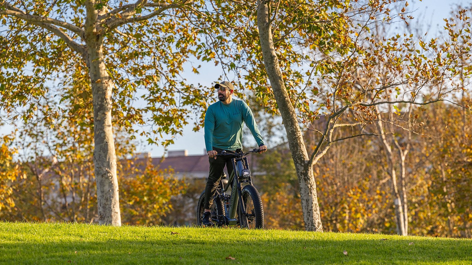Mann steht mit seinem E-Bike auf einer Wiese in einem herbstlichen Park mit goldenem Laub