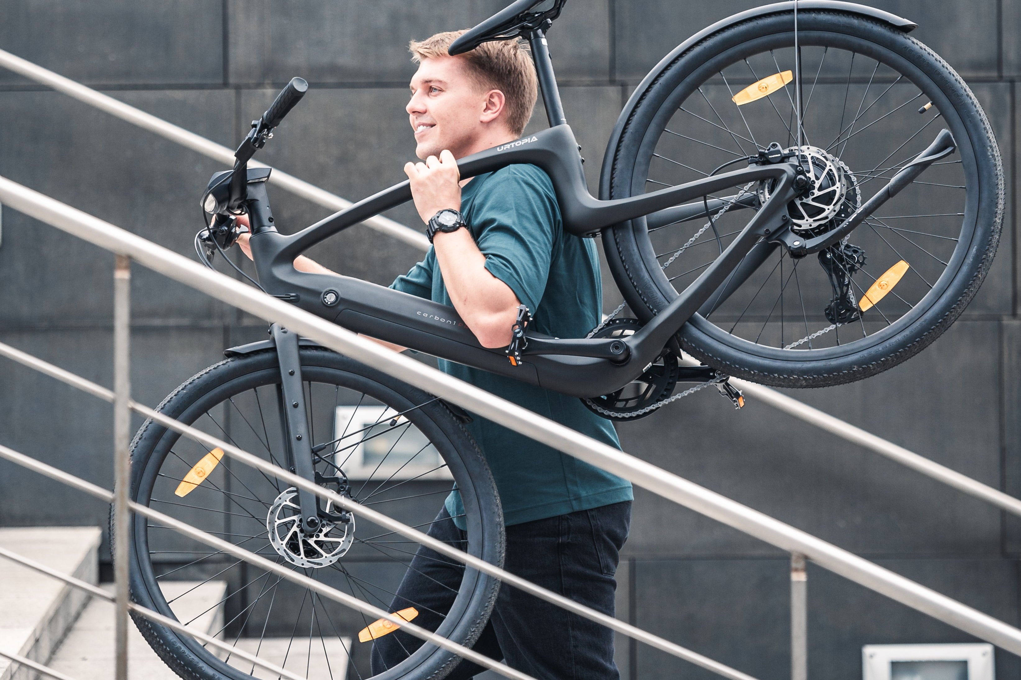 Person trägt den leichten Urtopia Carbon 1 Pro über der Schulter eine Treppe hinauf