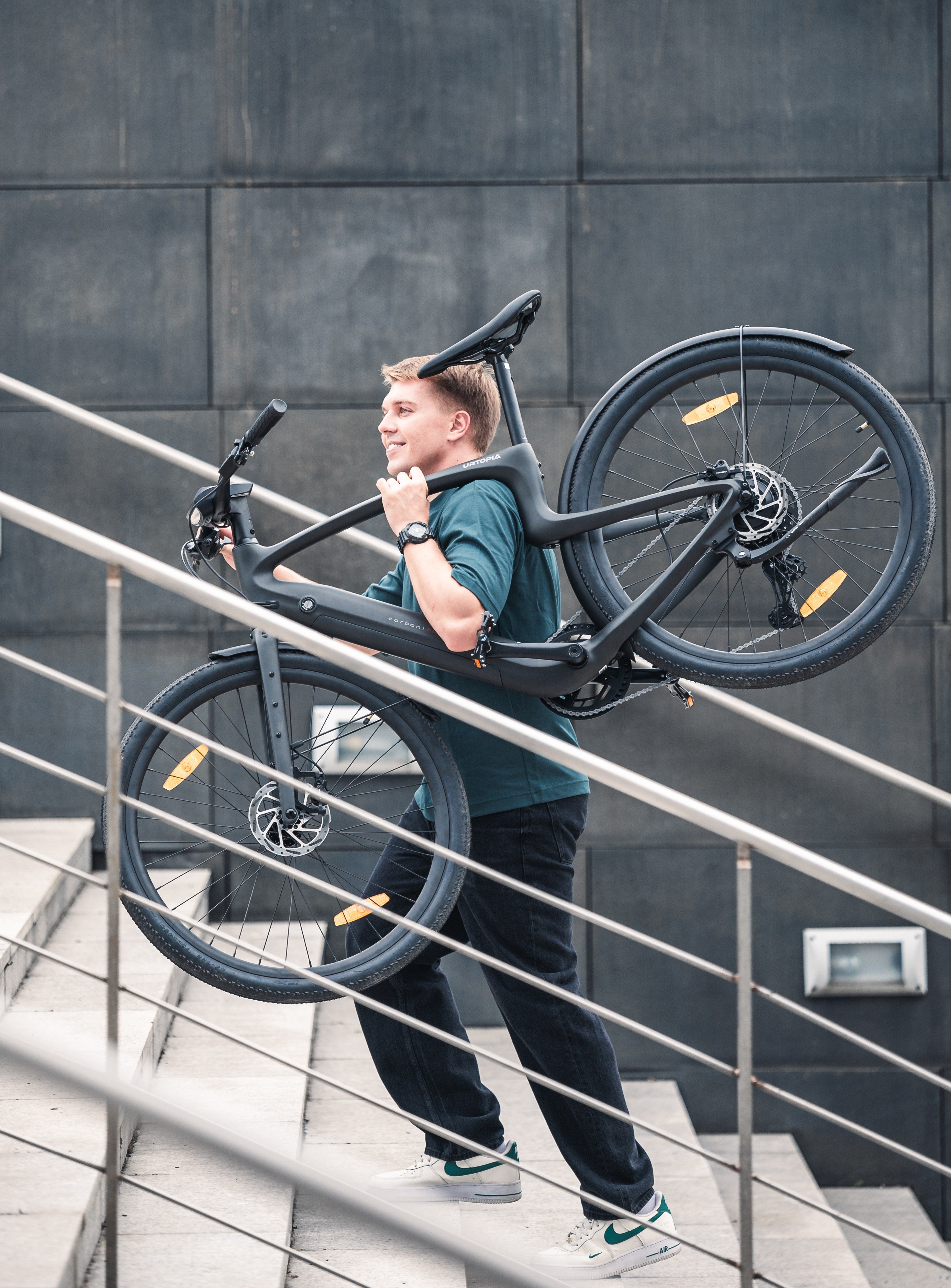 Person trägt den leichten Urtopia Carbon 1 Pro über der Schulter eine Treppe hinauf