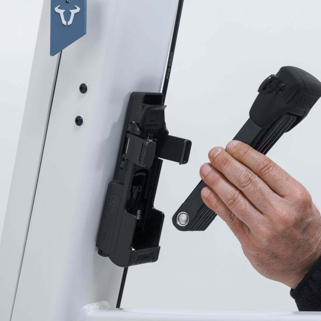 Hand attaching ABUS Bordo 6000K Faltschloss to Fidlock mount on VIA E-Lastenrad for secure locking.