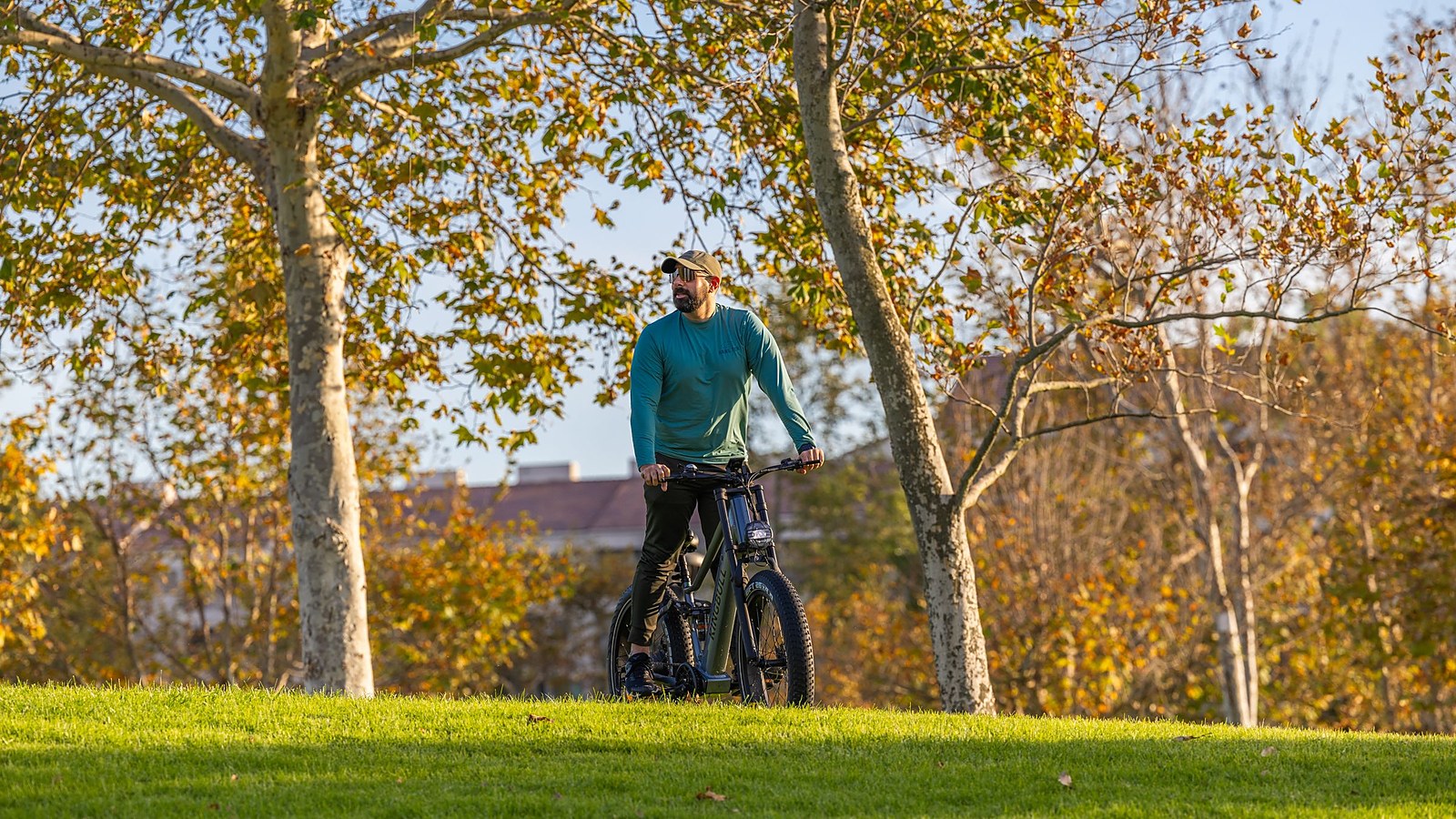 Mann steht mit seinem E-Bike auf einer Wiese in einem herbstlichen Park mit goldenem Laub